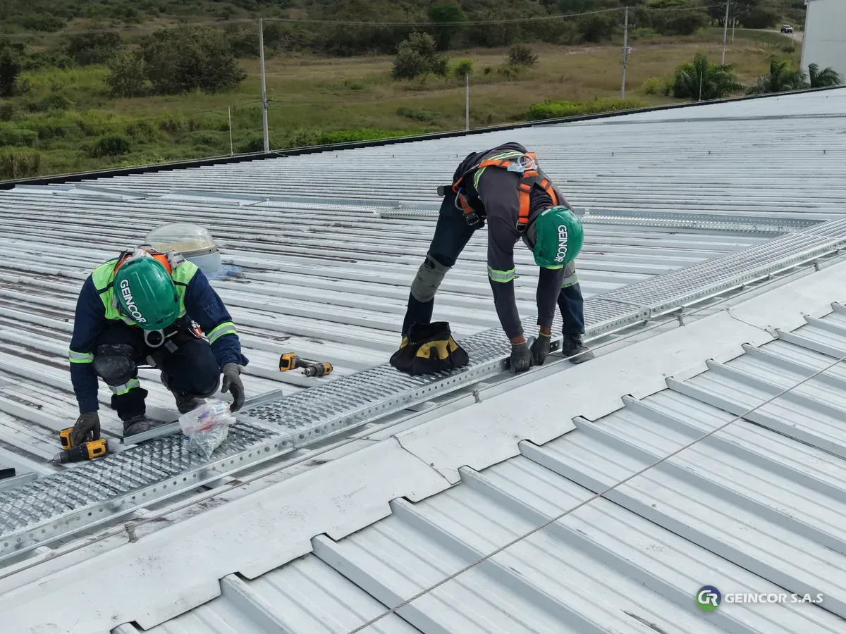 Tres técnicos con arnés, casco y eslinga conectada trabajando sobre una cubierta metálica, vistos desde el dron.