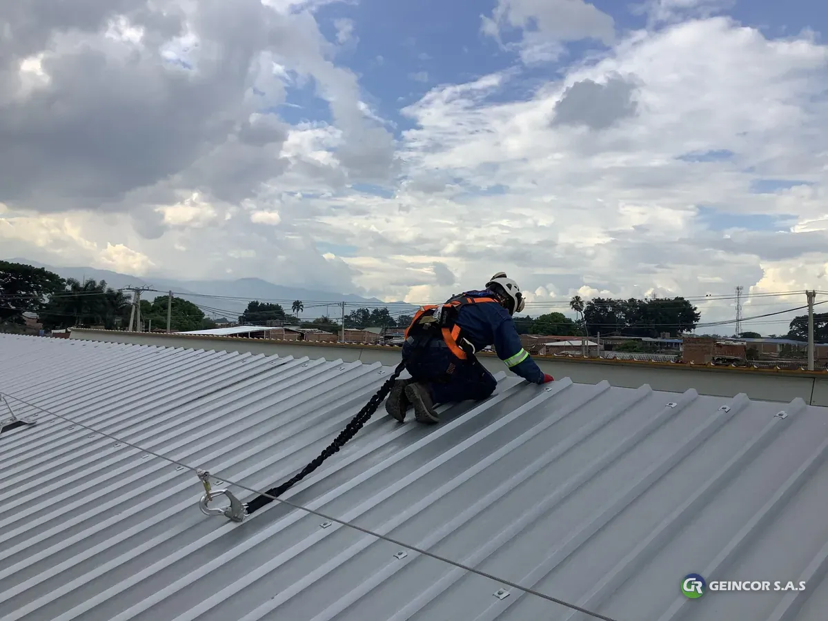 Técnico con arnés naranja arrodillado sobre una cubierta metálica, con el cielo detrás.
