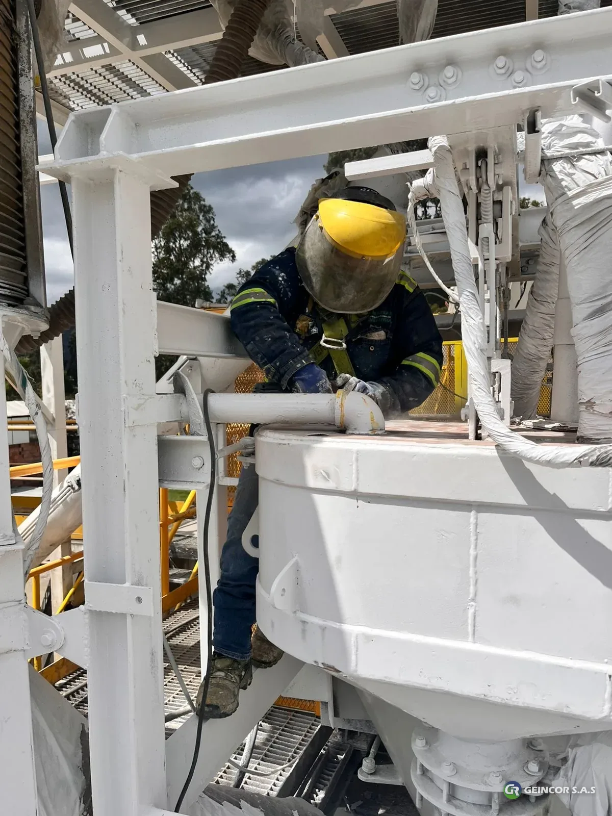 Técnico con arnés y careta trabajando en un equipo de una planta industrial